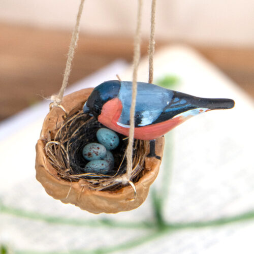 Handmade miniature bullfinch bird made from polymer clay on a walnut shell nest decoration